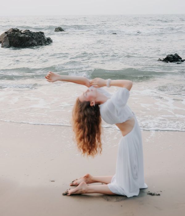 Woman gracefully performing a yoga pose outdoors at sunrise.